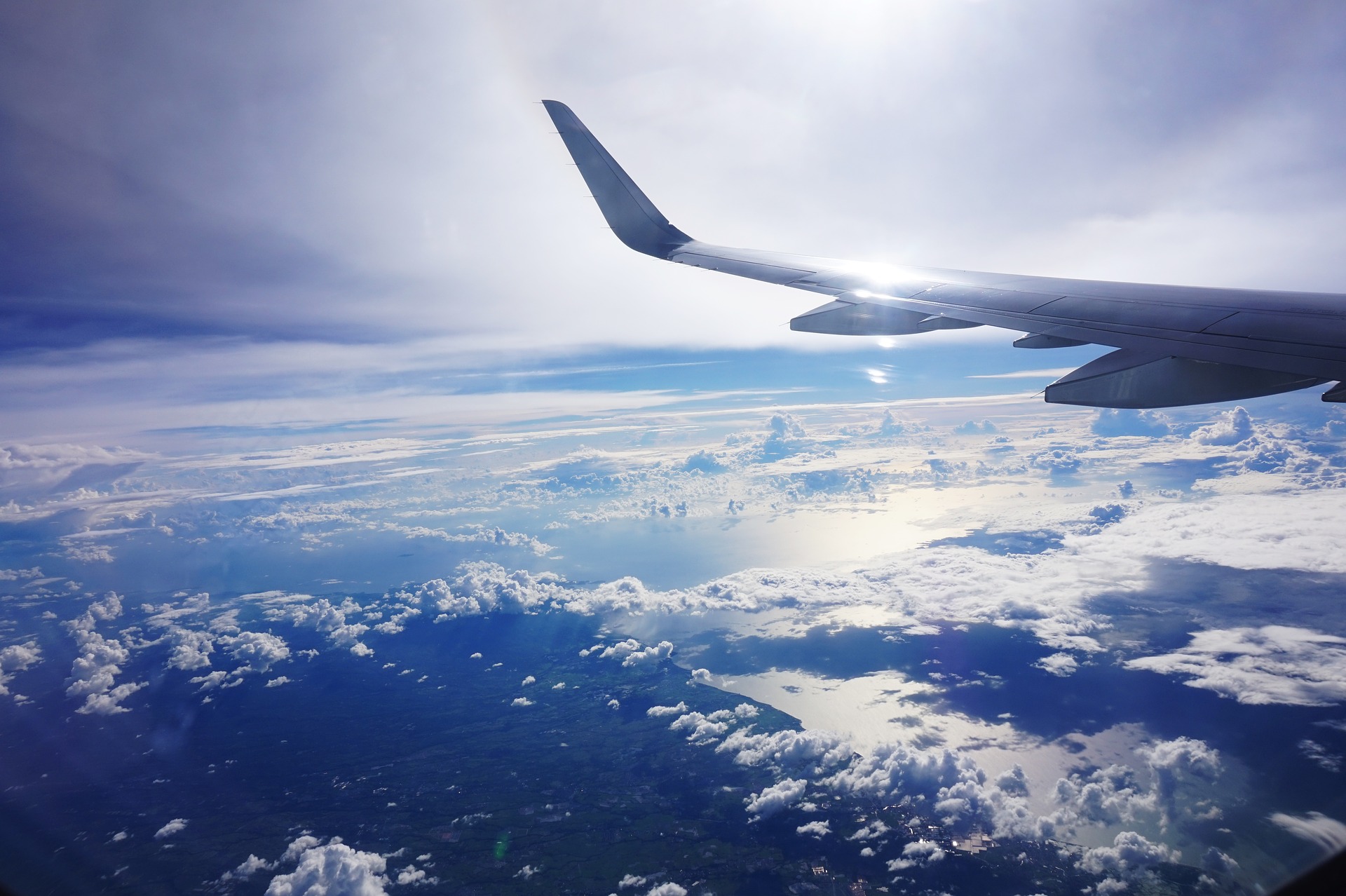 A plane wing is shown over clouds in the sky.