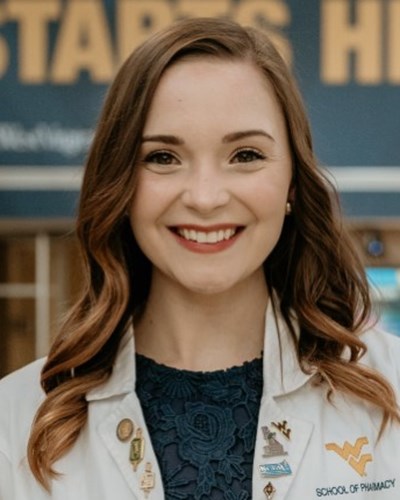 Samantha, wearing her WVU School of Pharmacy white coat, is standing in the Pylons lobby of the Health Sciences Center.