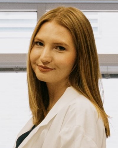 Kathryn is shown turning back towards the camera, in a lab setting, wearing a white coat.